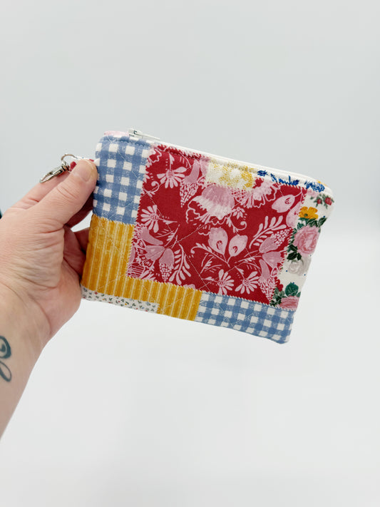 Hand holding a colorful floral gingham patchwork coin purse against a light gray background