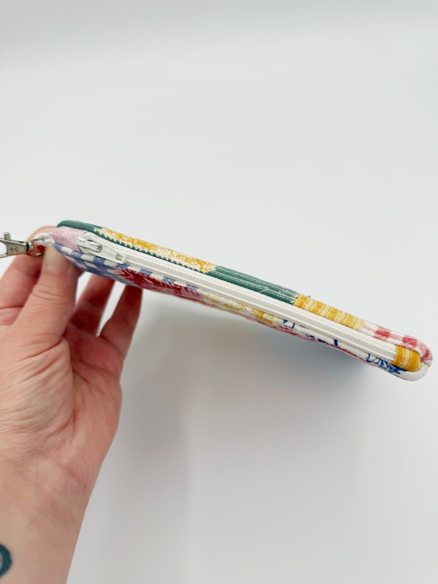 Hand holding a colorful fabric pouch against a white background showing white zipper closure