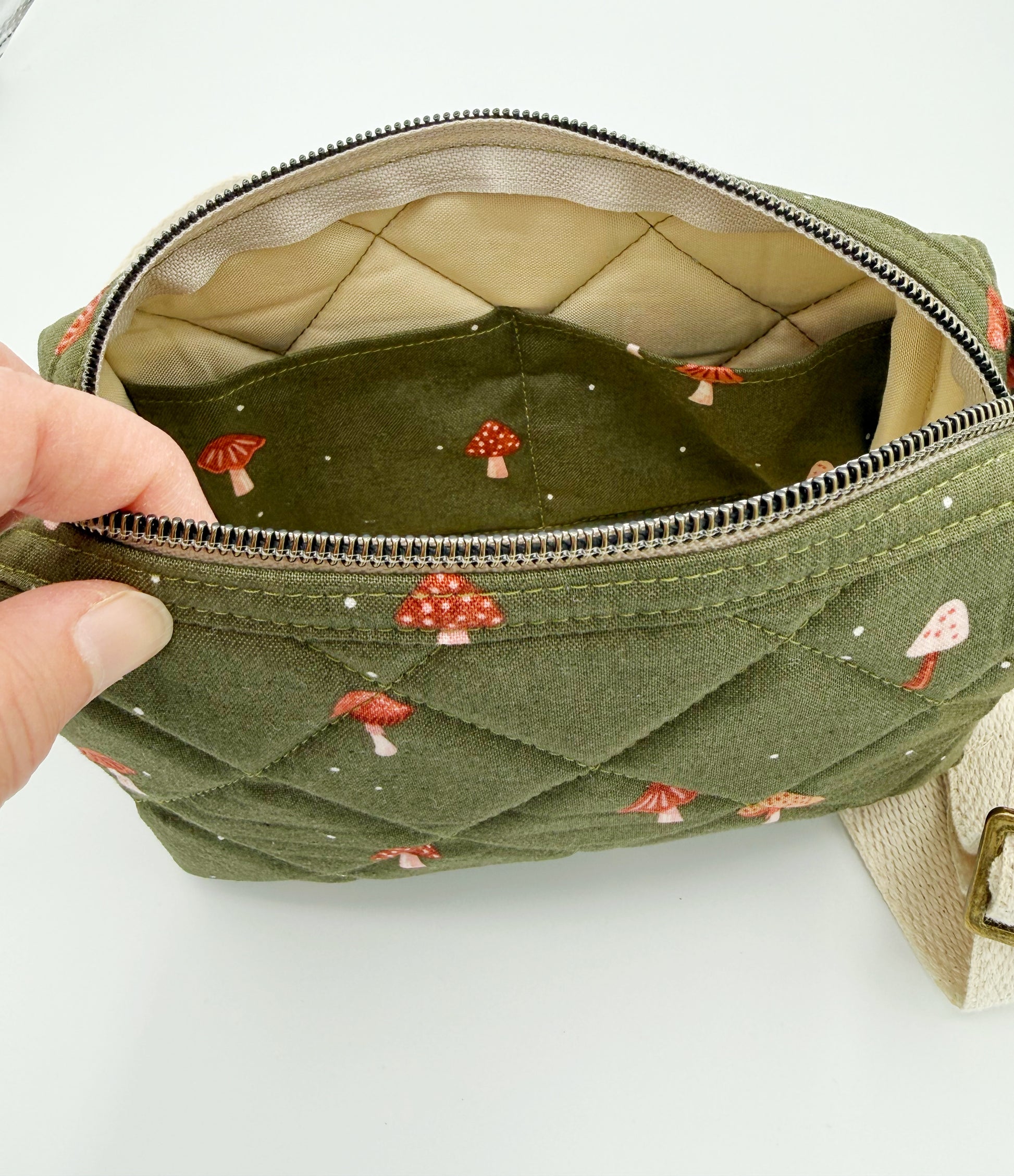 Green quilted bag with mushroom pattern held open by a hand on a white background