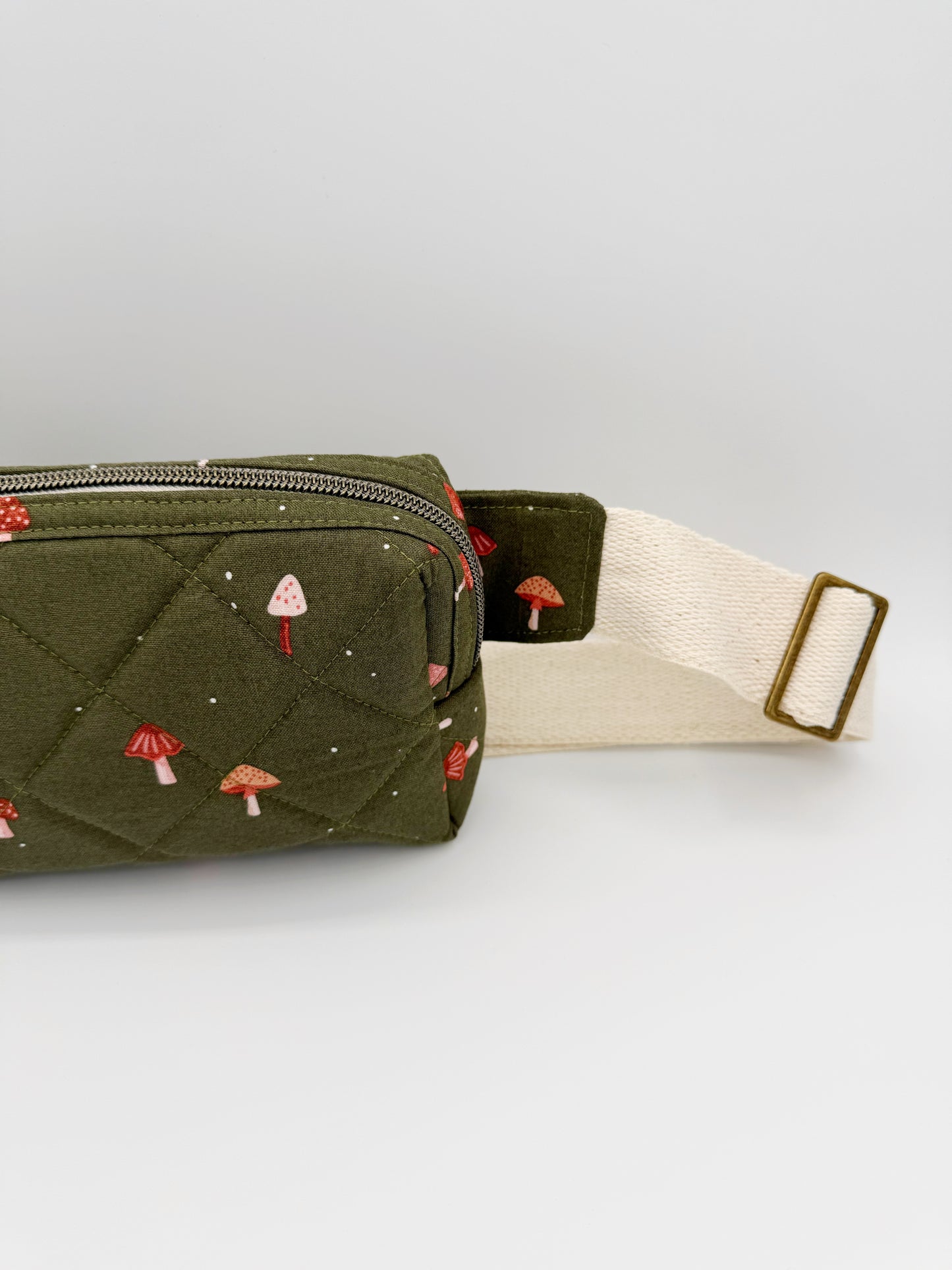 Green quilted bag with mushroom patterns on a white background right side view showing adjustable hardware