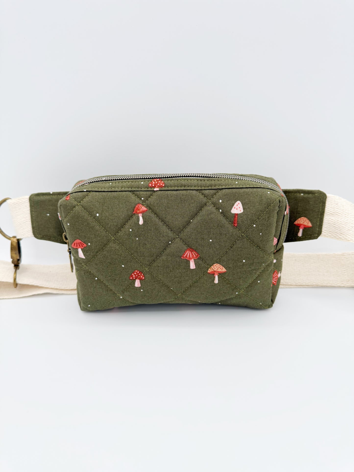 Green quilted fanny pack with mushroom pattern on a light gray background