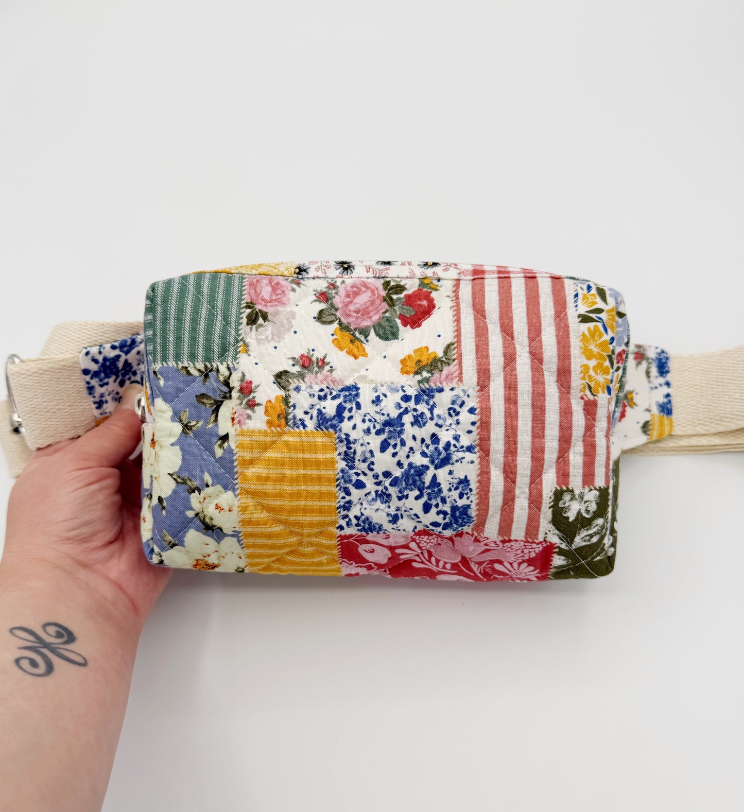 Patchwork-style belt fanny bag with floral and striped patterns held by a hand on a white background