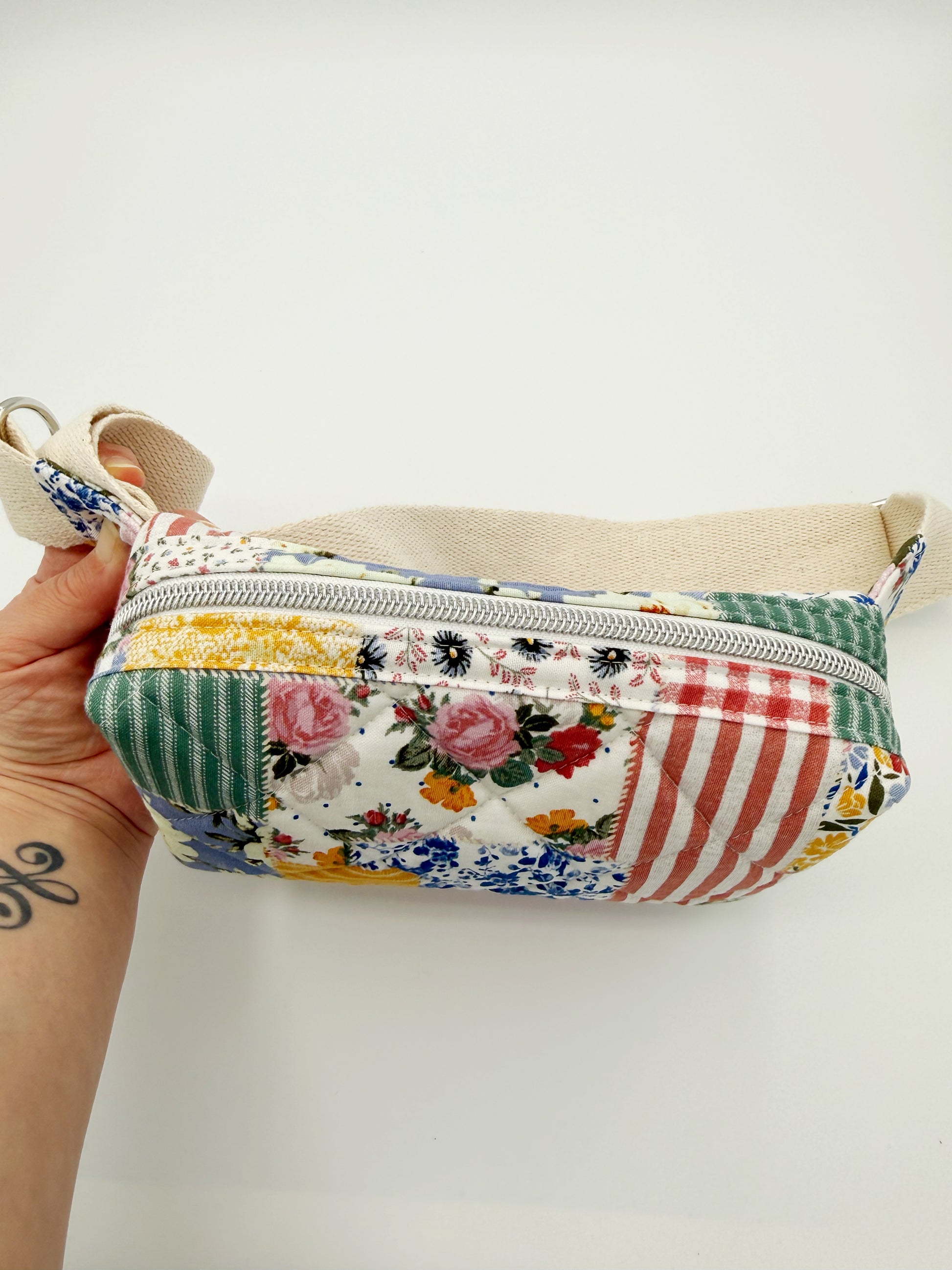 Patchwork-style pouch with floral and striped patterns held by a hand on a white background showing white zipper part of top of bag