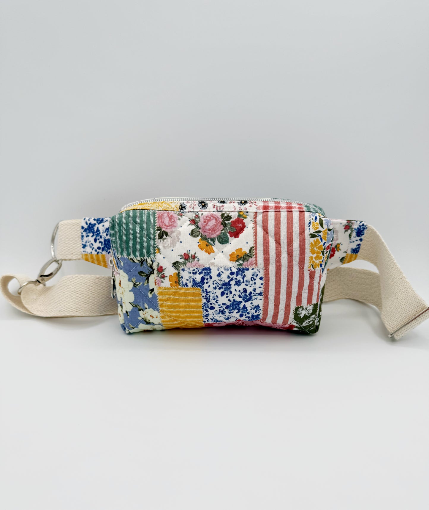 Patchwork-style crossbody fanny pack style bag with floral and striped patterns on a light gray background front view