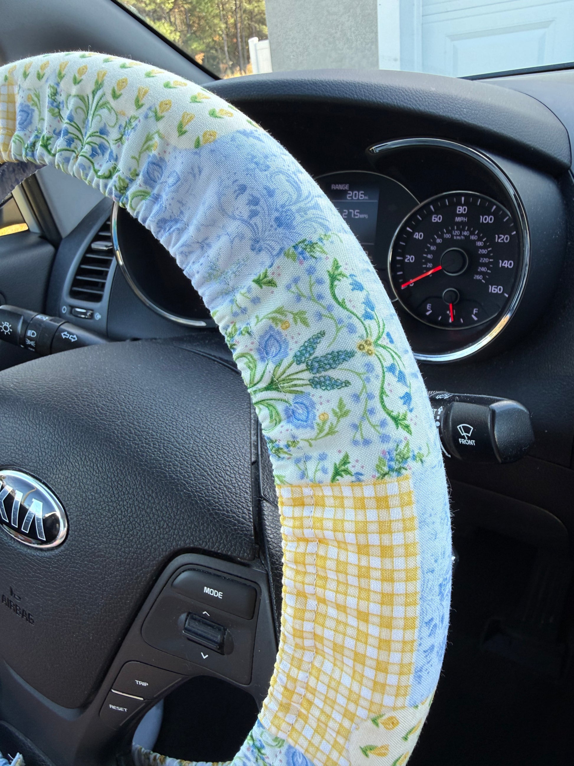 Car interior with a floral patchwork steering wheel cover and dashboard view.
