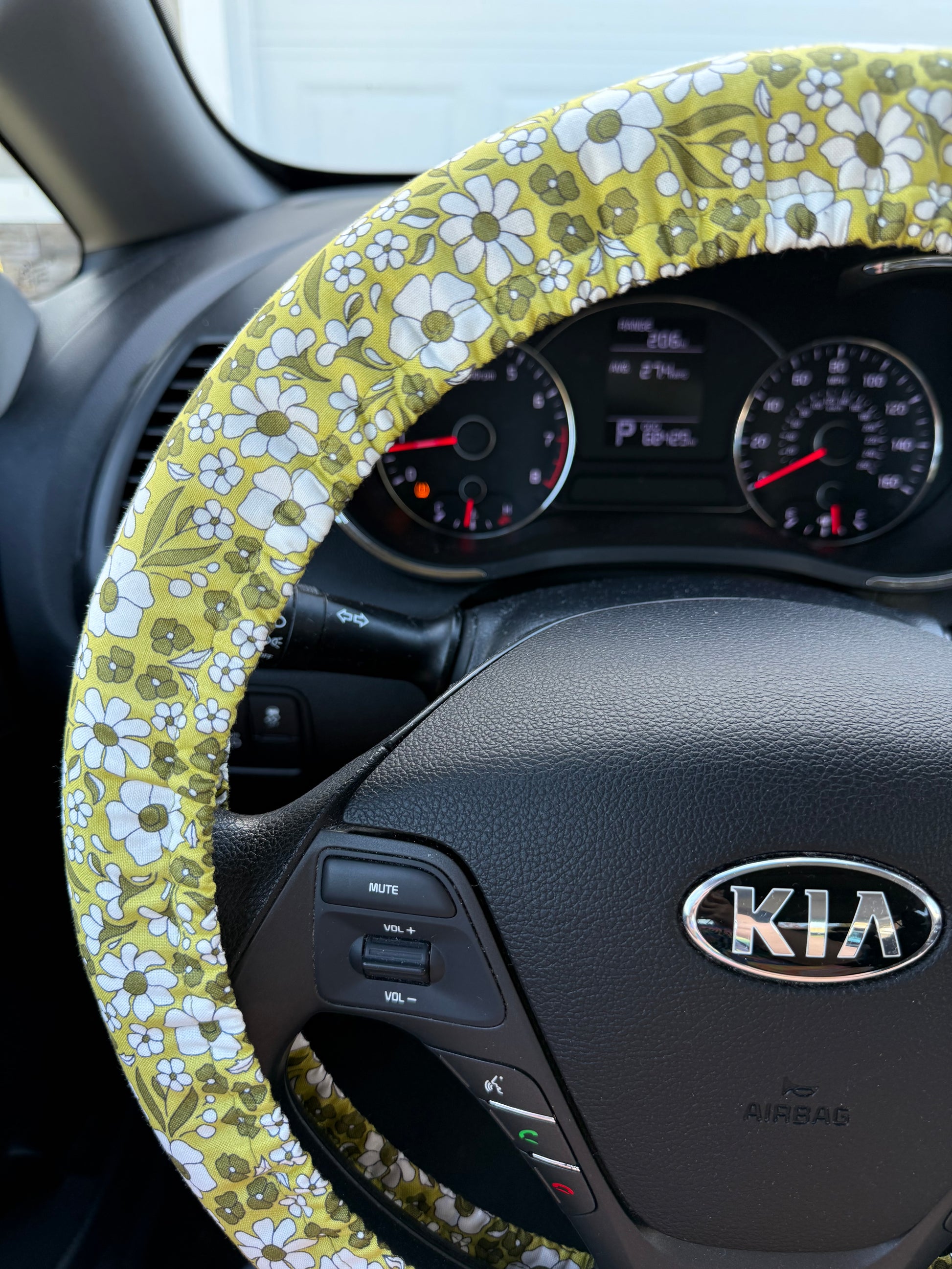 Steering wheel cover with a green floral pattern on a Kia car steering wheel left side view